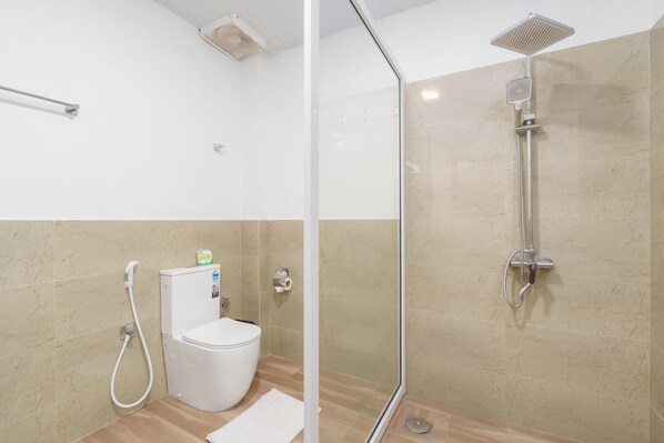 A bathroom with a toilet, a shower with a glass door, and beige tiled walls.
