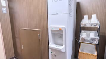 A hotel room with a white ice dispenser, a brown door, and a small wicker basket on a cart.