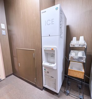 A hotel room with a white ice dispenser, a brown door, and a small wicker basket on a cart. - Smile Hotel Sasebo (Sasebo)