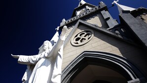 Una iglesia con una estatua de una figura vestida y una cruz en la parte superior.