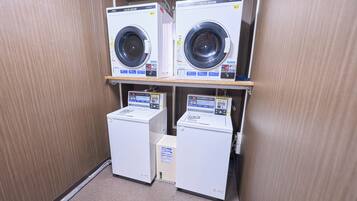 A laundry facility with two front-loading washing machines and two dryers, all with control panels and safety labels.