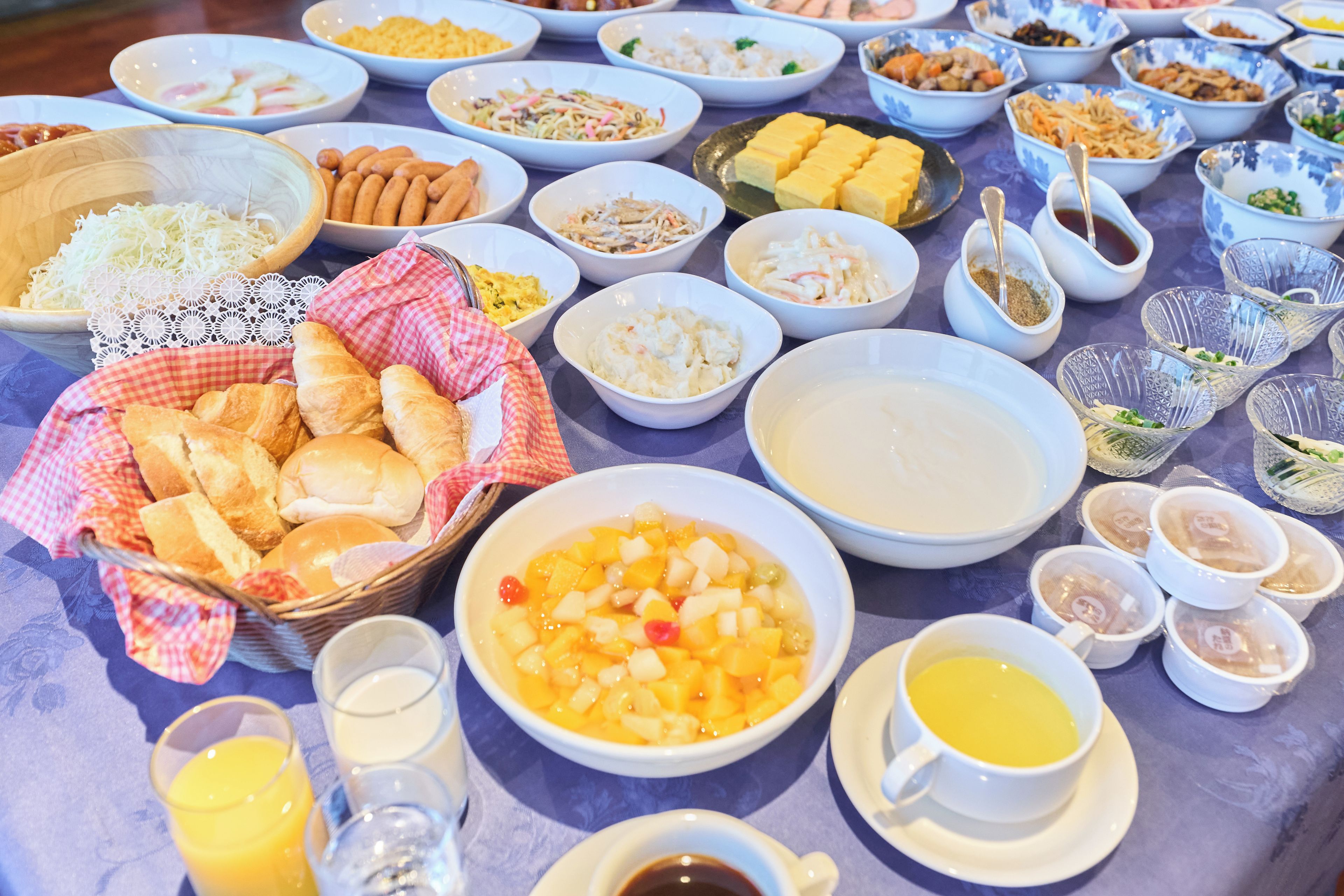 A table with various dishes, including a bowl of fruit salad, a plate of bread, and several small bowls of condiments.