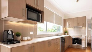 A modern kitchen with a coffee machine, microwave, oven, and a window with a view of greenery. - Driftwood in Blacksmiths - free WIFI, close to the beach (Blacksmiths)