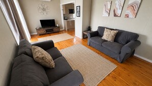 A living room with two grey sofas, a TV, a kitchen in the background, and abstract art on the wall. - Driftwood in Blacksmiths - free WIFI, close to the beach (Blacksmiths)