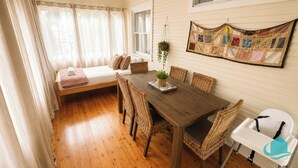 A cozy room with a wooden dining table, wicker chairs, a white bench, and a quilted wall hanging. - Driftwood in Blacksmiths - free WIFI, close to the beach (Blacksmiths)
