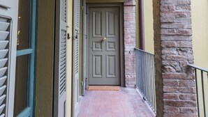 A corridor with a door at the end, a light fixture on the ceiling, and a brick column on the right. - Le Logge apartment (Parma)