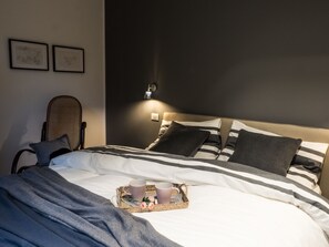 Ein ordentlich bezogenes Bett mit gestreifter Bettwäsche, ein Nachttisch mit Lampe und ein Tablett mit Tassen und Blumen auf dem Bett.