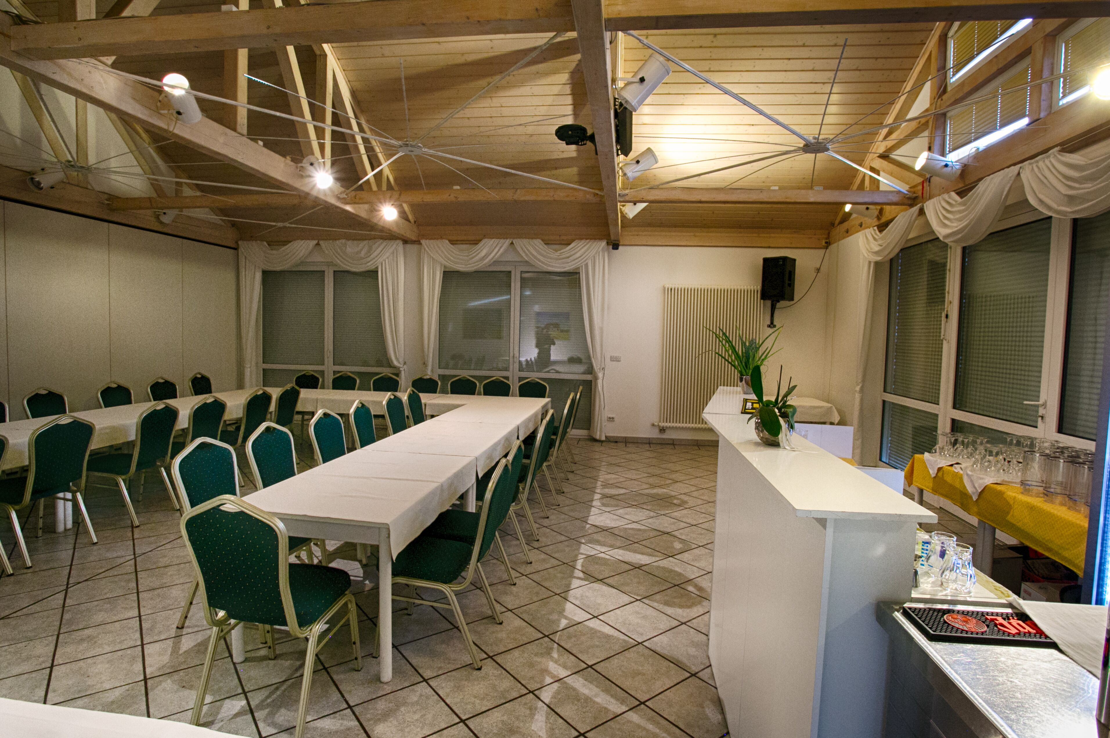 A conference room with a long table, green chairs, a white counter with glasses, and a ceiling fan.