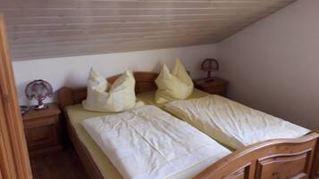 Ein Einzelbett mit Holz-Kopf- und Fußteil, zwei Nachttische mit Lampen sowie eine schräge Decke.