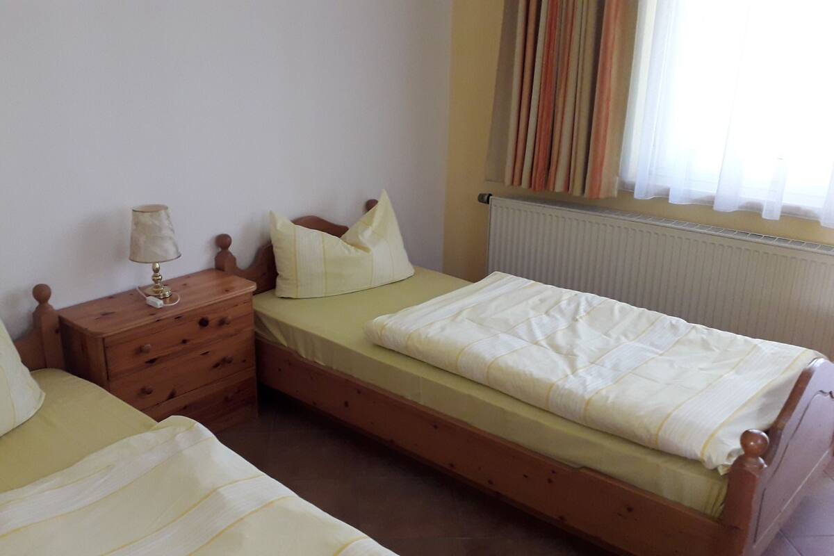 A bedroom with two single beds, a wooden nightstand with a lamp, and a radiator.