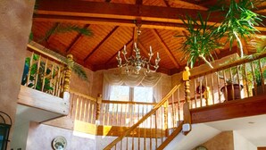 A wooden staircase with a chandelier, a reception desk, and potted plants. - Hotel Rosengarten (Naunhof)