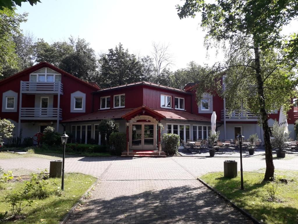 Um edifício vermelho com entrada central, cercado por vegetação e um caminho pavimentado.