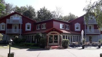 Un bâtiment rouge avec une entrée centrale, de nombreuses fenêtres et un petit jardin agrémenté de bancs.
