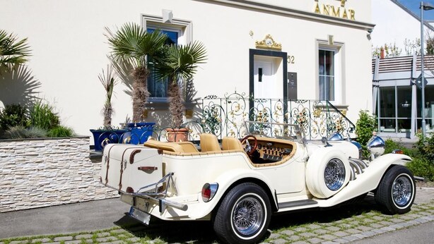 Un coche descapotable antiguo estacionado frente a un edificio blanco con el nombre "ANMAR" a la vista.