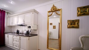 Cocina compacta con muebles blancos, encimera negra y espejo con marco dorado.