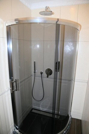 Une cabine de douche moderne dotée d’une porte en verre, d’un pommeau de douche à main et d’un panneau de commande.