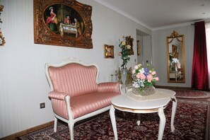 Une pièce avec un canapé recouvert d’un tissu rose, une table ronde blanche ornée d’un vase de fleurs et un grand miroir décoratif.