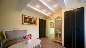 Una habitación con un sofá, una mesita con un jarrón de flores, un cuadro en la pared, un espejo y un armario.