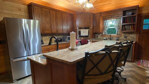 A kitchen with wooden cabinets, a stainless steel refrigerator, a central island with chairs, and a hanging light fixture. - Peace of Heaven - close to everything you'll want to see and do! (Broken Bow)
