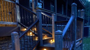 A wooden staircase with railings and lights, leading to a porch with stone walls and a wooden deck. - Peace of Heaven - close to everything you'll want to see and do! (Broken Bow)