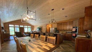 A spacious kitchen with wooden cabinets, a large dining table, and a herringbone-patterned floor. - Peace of Heaven - close to everything you'll want to see and do! (Broken Bow)