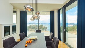 A modern dining area with a large table, chairs, and a view of the sea.