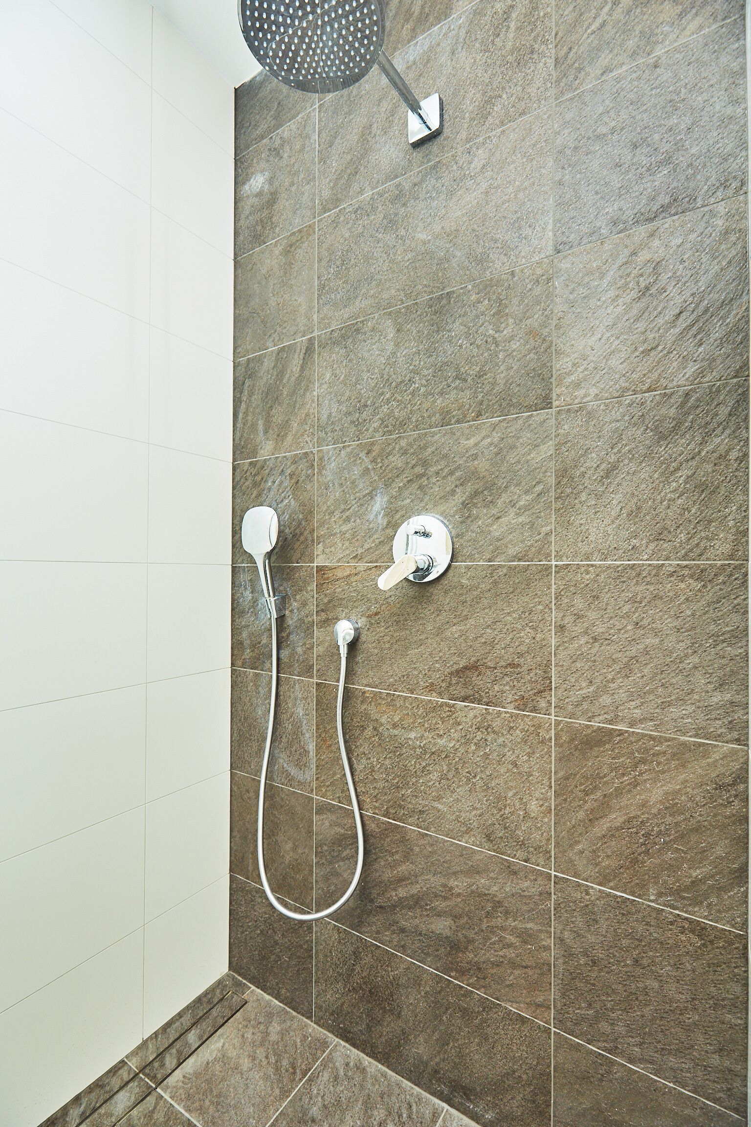 Ein Duschbereich mit Handbrause und am Wand montiertem Wasserhahn.