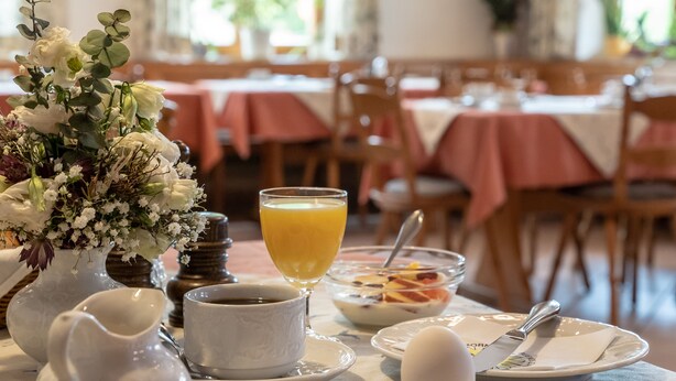 A breakfast setting with a table set for two, including a vase of flowers, a glass of orange juice, a bowl of cereal, and a plate with a knife and fork. - Gasthof Zur frohen Einkehr (Ohrenbach)