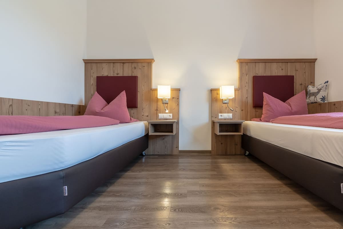 A double room with two beds, wooden headboards, bedside tables, and wall-mounted lamps.