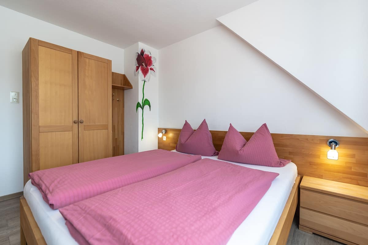 A bedroom with a large bed, wooden wardrobe, and a wall-mounted light fixture.