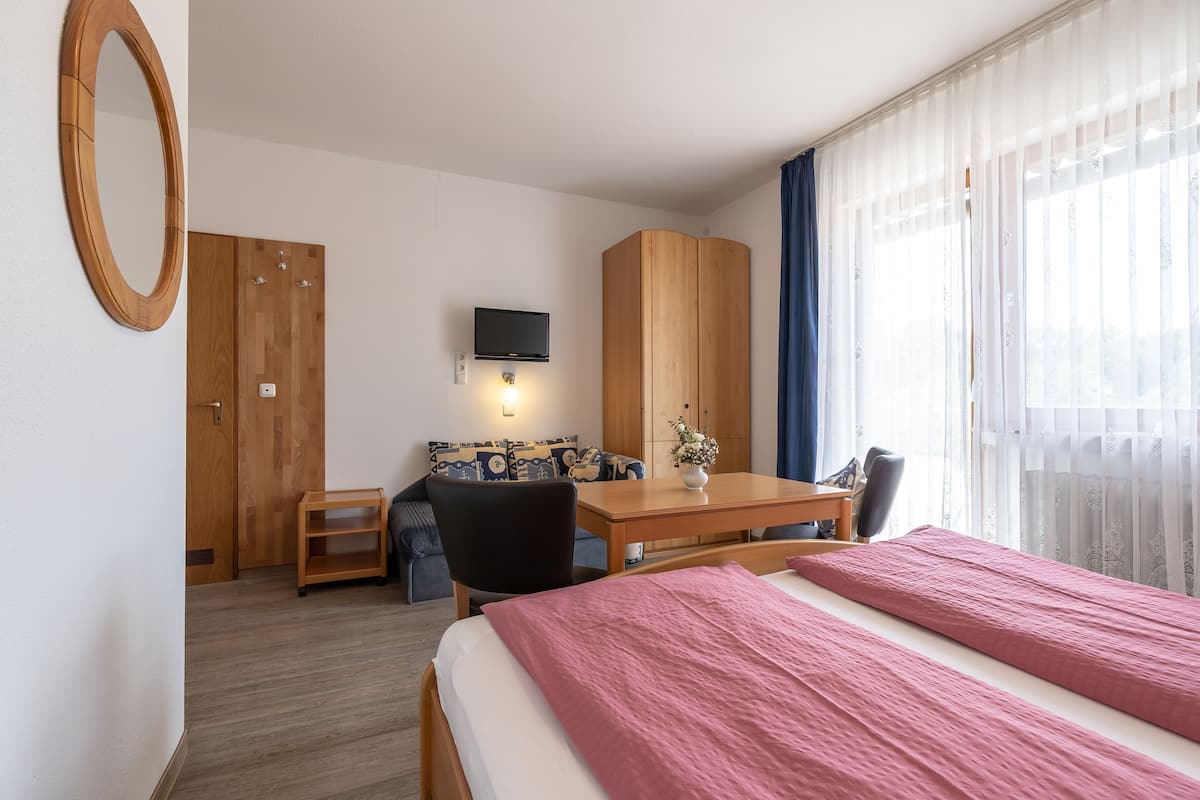 A hotel room with a bed, a desk, a chair, a TV, a wardrobe, and a window with curtains.