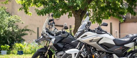 Dos motocicletas estacionadas en una calle adoquinada, con un edificio y árboles de fondo.