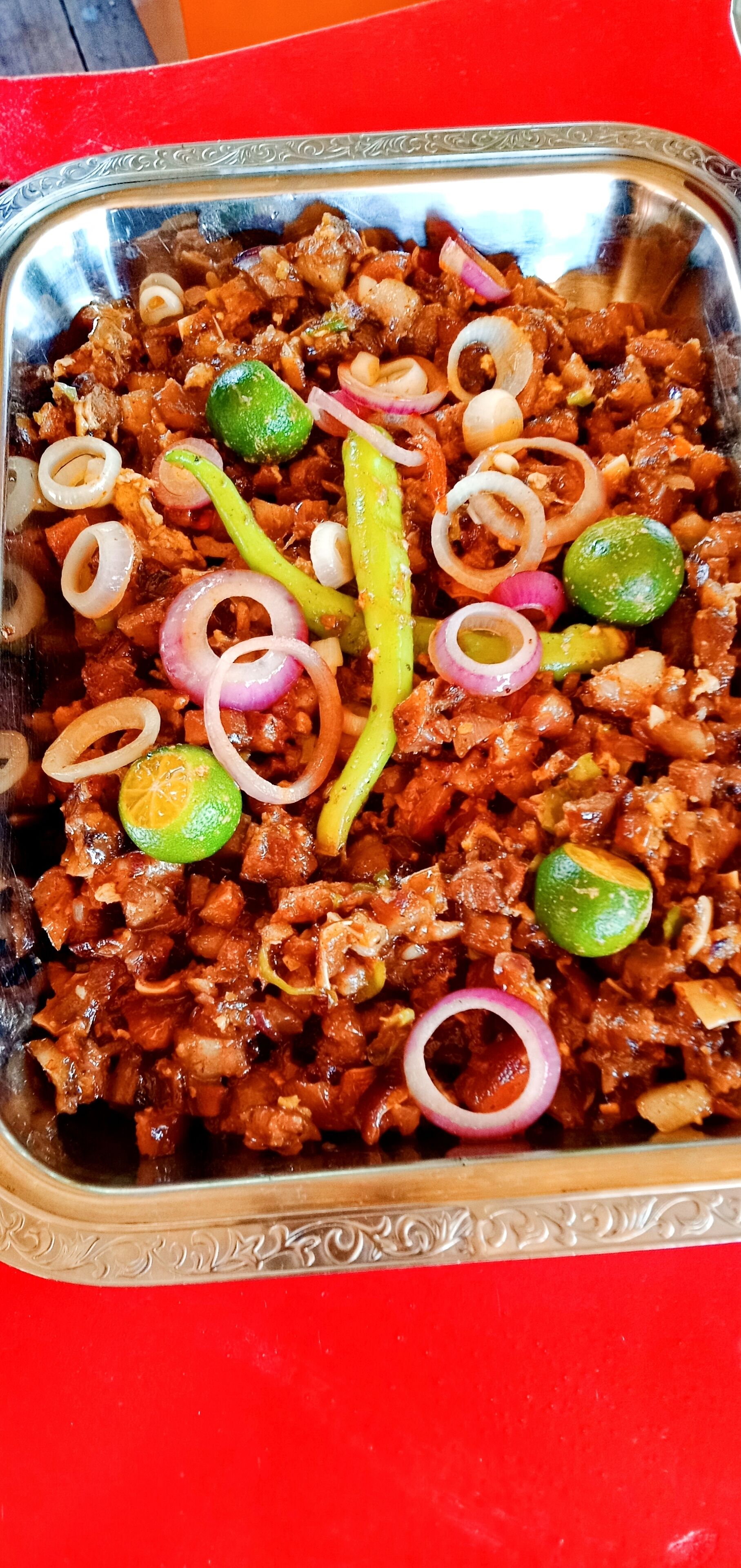 Una fuente de acero inoxidable llena de carne adornada con lima, cebollas y chiles verdes.