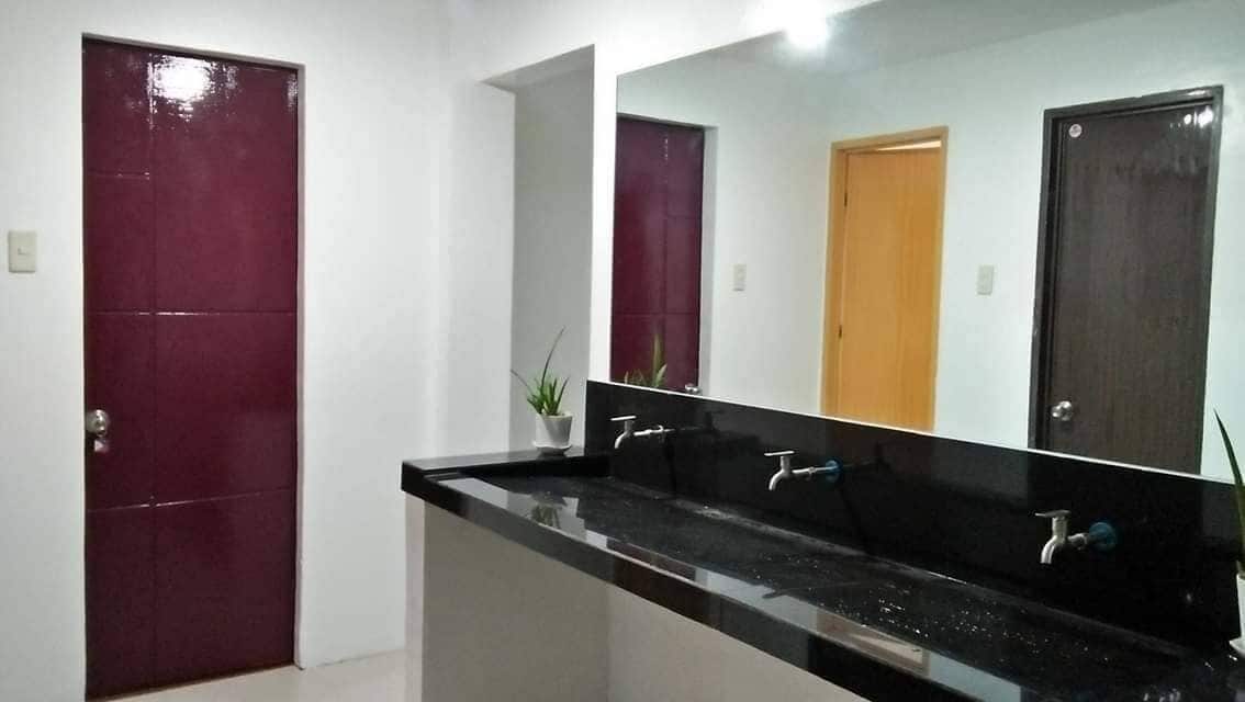 Une salle de bain avec un lavabo noir, deux robinets et un miroir. Il y a trois portes : une de couleur bordeaux, une en bois et une de couleur marron foncé.