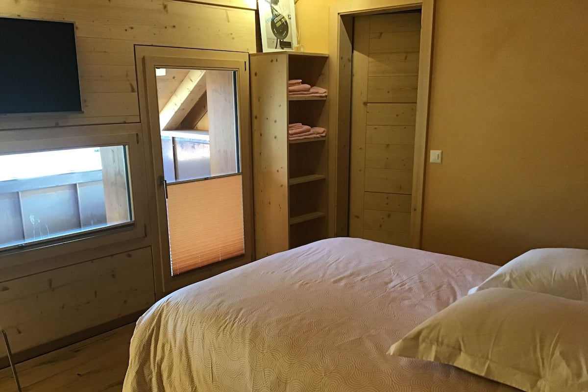 Ein Schlafzimmer mit einem Bett, einem Fenster, einem Holzschrank und einem Regal mit gefalteten Handtüchern.