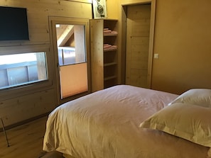 Un dormitorio con una cama, una ventana, un armario de madera y una estantería con toallas dobladas.