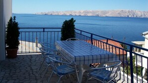 Ein Balkon mit Tisch und Stühlen mit Blick auf ein Gewässer und hügeliges, felsiges Gelände.