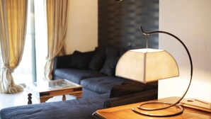 Een moderne woonkamer met een donkere bank, een houten salontafel en een lamp met een opvallend ontwerp.