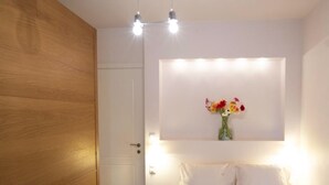 Een slaapkamer met een houten garderobe, een bed met witte beddengoed, een wandlamp en een vaas met bloemen.
