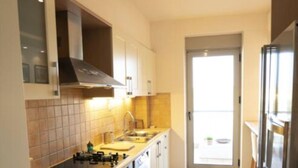 Een smalle keuken met een ingebouwde oven, een wasmachine en een koelkast.
