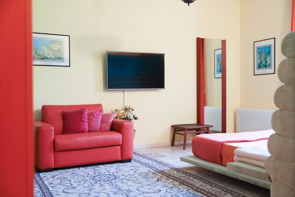 Una camera da letto moderna con un divano rosso, una TV a schermo piatto, un letto con copriletto rosso e un piccolo tavolo con un vaso di fiori.