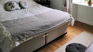 Een slaapkamer met een bed, nachtkastje, lamp, ingelijste foto’s en een raam met gordijnen.