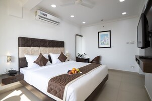 A hotel room with a large bed, a bedside table with a phone, a nightstand, a TV, and a framed picture on the wall.