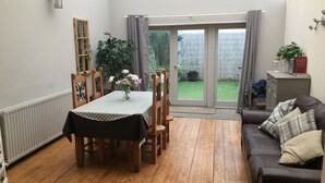 A dining area with a table and chairs, a wooden floor, a sofa, and a view of the garden through a glass door. - Large 2-bed House Derbyshire off Chatsworth rd (Chesterfield)