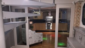 A modern kitchen with a built-in oven, a dining area with a patterned sofa, and a brick wall. - Large 2-bed House Derbyshire off Chatsworth rd (Chesterfield)