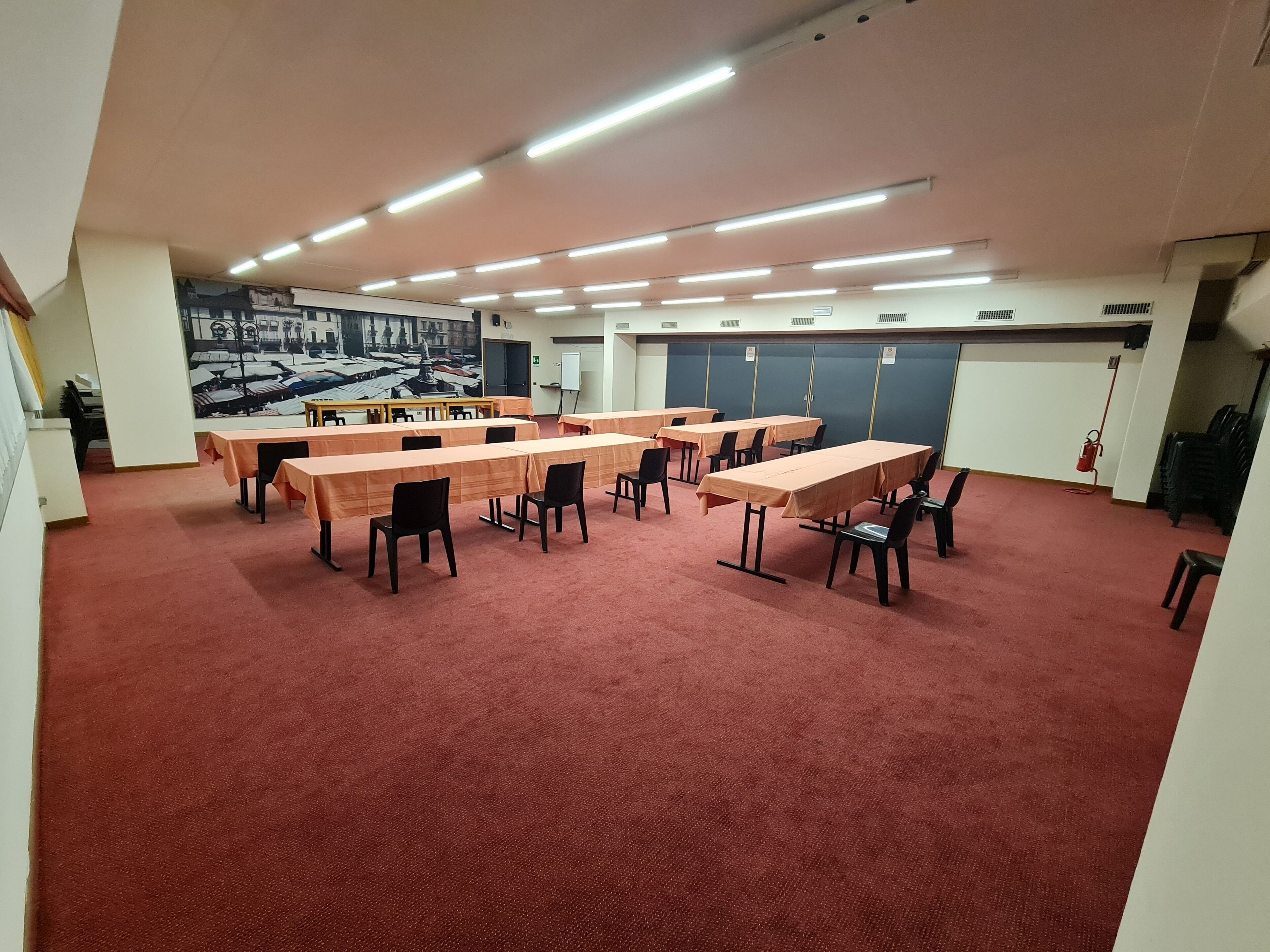 Une salle de conférence dotée de plusieurs tables et chaises, d’un sol recouvert d’un tapis rouge et d’une fresque murale.