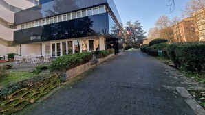 Un edificio moderno con fachada de vidrio, un sendero pavimentado y un pequeño espacio al aire libre con sillas.