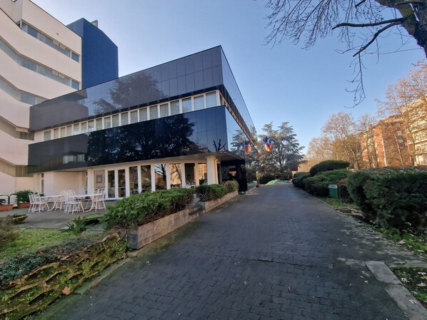 A modern building with a glass facade, a paved walkway, and a small outdoor seating area with chairs.