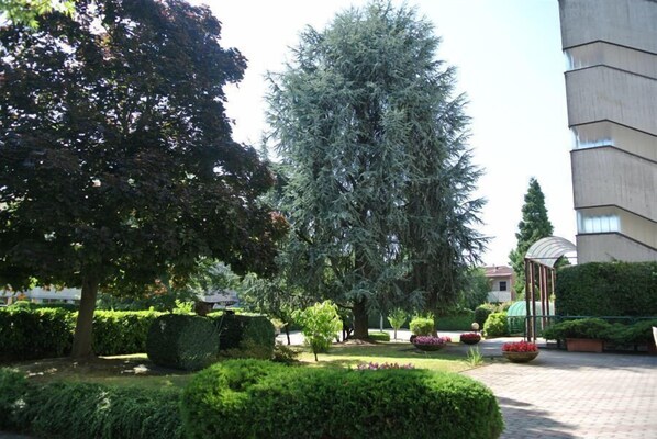 A landscaped garden with various trees and shrubs, a gazebo, and a building in the background.