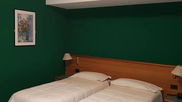 A hotel room with two beds, a nightstand, a lamp, and a painting on the wall.